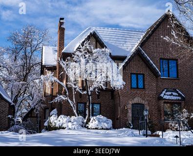 Una casa in stile revival Tudor con tetto spiovente, mezza pietra e alto camino in una splendida giornata invernale coperta da neve appena caduta. Foto Stock
