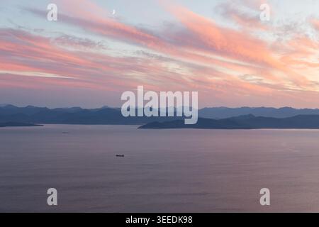 Ampia vista panoramica della baia di Avacha all'alba con nuvole rosa, mare calmo, piccola nave e sagome di montagna a strati, Kamchatka Krai, Russia Foto Stock