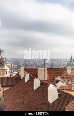 Vista degli storici tetti di tegole rosse con camini fumanti che si affacciano sul paesaggio urbano sotto un cielo nuvoloso Praga, Praga, Cechia. Foto Stock