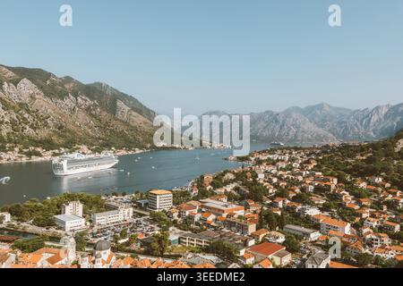 Ampia vista panoramica su Cattaro, la baia di Cattaro e le montagne circostanti in Montenegro, con una grande nave da crociera in acque calme e un paesaggio urbano con tetto rosso in su Foto Stock