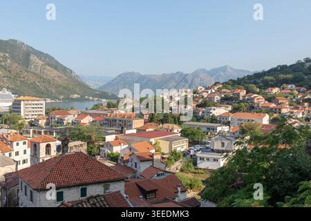 Vista panoramica sopraelevata sui tetti di tegole rosse e sugli edifici in pietra a Cattaro, con la baia di Cattaro e le aspre montagne sullo sfondo, Montenegro Foto Stock