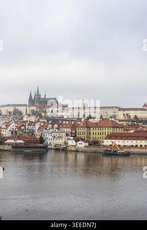 Vista del Castello di Praga e degli storici edifici dal tetto rosso lungo il fiume Moldava sotto un cielo coperto a Praga, Praga, Cechia. Foto Stock