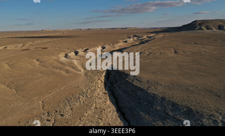 Una prospettiva aerea rivela un profondo canyon drammatico che si estende su un vasto e arido paesaggio desertico sotto un cielo azzurro limpido con nuvole sparse Foto Stock