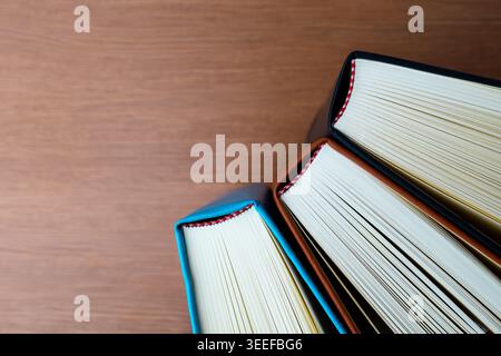 Un primo piano ad alto angolo di tre libri in copertina rigida disposti a ventaglio su una superficie in legno. Educazione, biblioteca, letteratura. Foto Stock