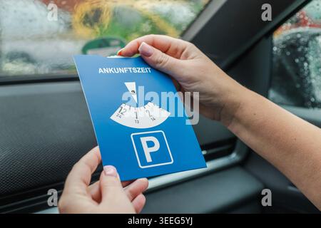Donna che tiene il disco del parcheggio europeo all'interno dell'auto durante il giorno di pioggia Foto Stock
