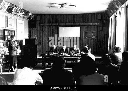 Slaviansk, 1983. Sala conferenze della fabbrica di isolatori per armature (AIZ). Un oratore si trova sul podio, rivolgendosi al pubblico e al presidio seduti al tavolo durante una riunione ufficiale. Questa fotografia vintage in bianco e nero cattura l'atmosfera autentica dell'epoca, riflettendo le attività quotidiane e la cultura industriale della regione durante il periodo sovietico. Funge da prezioso documento storico della comunità locale, preservando la memoria visiva delle persone e della loro vita quotidiana, mostrando un tranquillo Donbas. Foto Stock