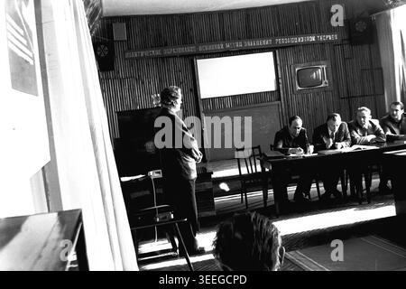 Slaviansk, 1983. Sala conferenze della fabbrica di isolatori per armature (AIZ). Un uomo sta sul podio tenendo un discorso vicino al tavolo del presidio, visto dal punto di vista del pubblico seduto. Questa fotografia vintage in bianco e nero cattura l'atmosfera autentica dell'epoca, riflettendo le attività quotidiane e la cultura industriale della regione durante il periodo sovietico. Funge da prezioso documento storico della comunità locale, preservando la memoria visiva delle persone e della loro vita quotidiana, mostrando un tranquillo Donbas. Foto Stock
