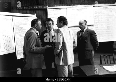 Slaviansk, 1983. Sala conferenze della fabbrica di isolatori per armature (AIZ). Quattro uomini in tute formali stanno insieme impegnati in una conversazione profonda, probabilmente in rete durante una pausa in un evento ufficiale. Questa fotografia vintage in bianco e nero cattura l'atmosfera autentica dell'epoca, riflettendo le attività quotidiane e la cultura industriale della regione durante il periodo sovietico. Funge da prezioso documento storico della comunità locale, preservando la memoria visiva delle persone e della loro vita quotidiana, mostrando un tranquillo Donbas. Foto Stock