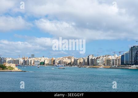Sliema, Malta - 16 maggio 2025: Ampia vista panoramica sul lungomare di Sliema, sul moderno skyline e sulle barche nel porto di Marsamxett sotto il suggestivo cielo nuvoloso di ma Foto Stock