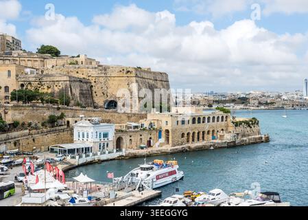 Sliema, Malta - 16 maggio 2025: Vista delle storiche fortificazioni in pietra, del porto turistico e dell'architettura sul lungomare lungo la costa mediterranea con barche e h Foto Stock
