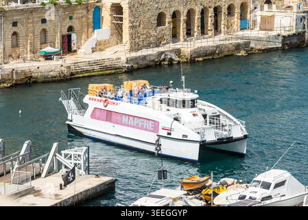 La Valletta, Malta - 16 maggio 2025: Traghetto da Sliema a la Valletta che naviga attraverso il porto storico, con i passeggeri sul ponte e l'architettura in pietra sul lungomare Foto Stock