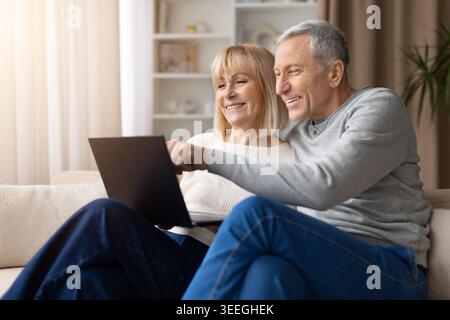 Coppia matura felice che utilizza il notebook a casa, sfogliando i contenuti online Foto Stock