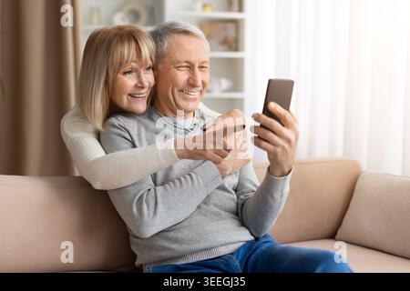 Felice coppia di anziani che utilizza lo smartphone a casa, godendo di una comunicazione video Foto Stock