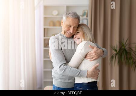Una coppia anziana amorevole che si abbraccia calorosamente a casa, esprimendo affetto Foto Stock