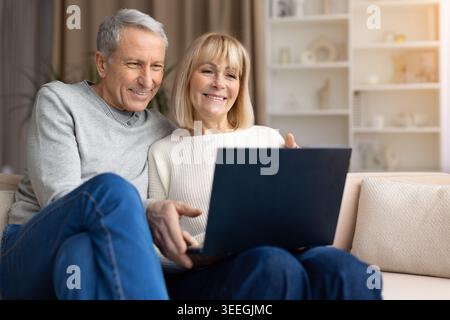 Coppia senior che si rilassa con un laptop sul divano di casa, navigando su Internet Foto Stock
