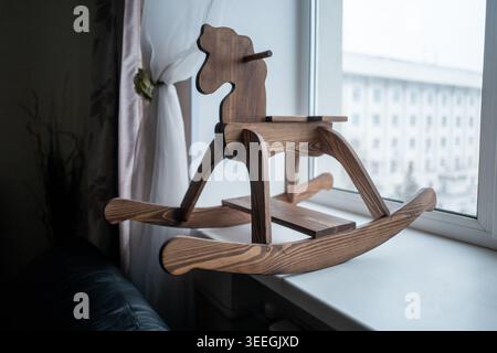 Un cavallo a dondolo in legno lavorato a mano poggia su un davanzale luminoso, che evoca nostalgici giochi d'infanzia e decorazioni rustiche in stile vivaio con calda venatura di legno. Foto Stock