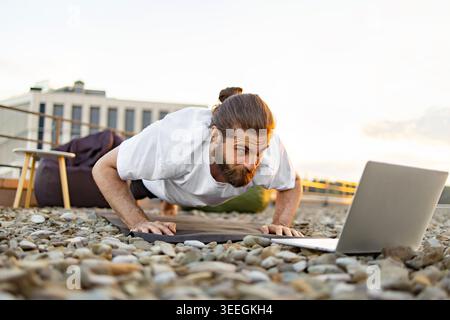 Uomo che fa pushup con notebook Foto Stock