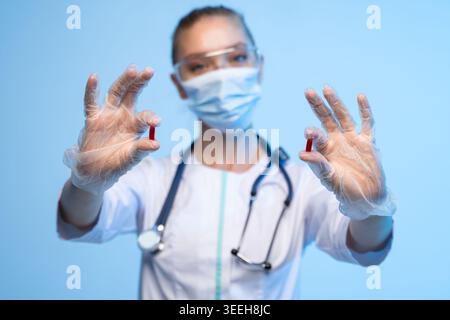 Operatore medico che indossa guanti, maschera e occhiali di sicurezza che tengono pillole rosse, concentrandosi sul trattamento, assistenza sanitaria e farmaci Foto Stock