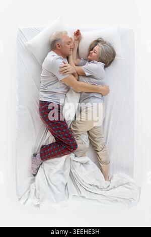 Una coppia anziana amorevole si coccola mentre dorme insieme nel letto bianco. Foto Stock