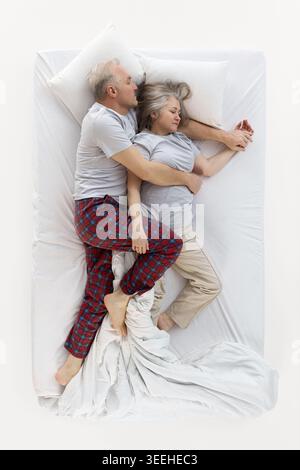 Uomo anziano che abbraccia la donna addormentata in posizione di spogliamento sul letto. Foto Stock