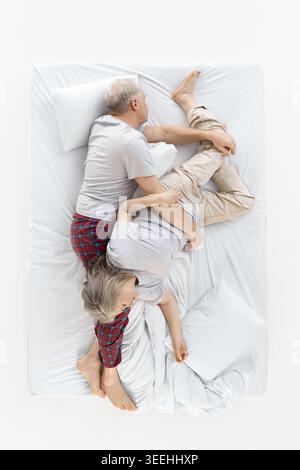 La coppia più anziana dorme in posa aggrovigliata sul letto bianco dall'alto. Foto Stock