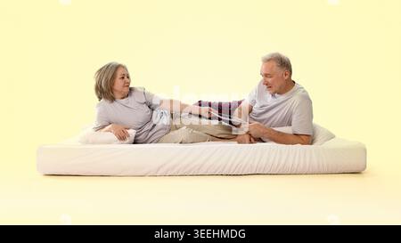 Una donna anziana che consegna un giornale all'uomo mentre si rilassa sul letto in un ambiente giallo pastello Foto Stock