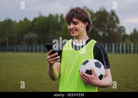 Tennista molto giovane in piedi sul campo usando lo smartphone durante la pausa in allenamento. Foto Stock