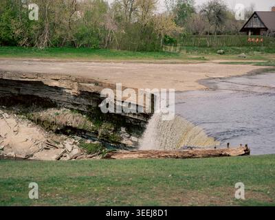 L'acqua scorre sull'ampia cascata di Jägala con un tronco intempestivo sul bordo, il fiume Jägala, Estonia, in primavera Foto Stock