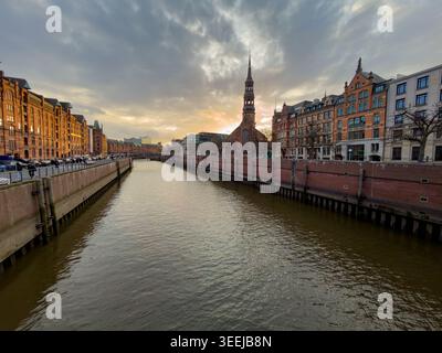 AMBURGO, GERMANIA - 28 MARZO 2026: La guglia della chiesa di Santa Caterina si erge in alto contro un suggestivo cielo al tramonto che si affaccia su un canale nella storica Chiesa Di Santa Caterina Foto Stock