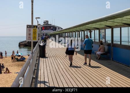 Persone che camminano sul molo di Bournemouth, Dorset, in Inghilterra: Rilassata passeggiata sul mare sotto il cielo azzurro. Foto Stock