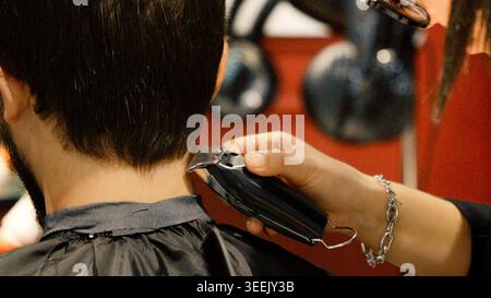 Primo piano del barbiere che taglia i capelli dell'uomo con il regolacapelli elettrico per professionisti ... Foto Stock