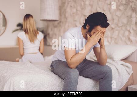 Un uomo siede sul bordo di un letto con le mani che coprono il viso Foto Stock