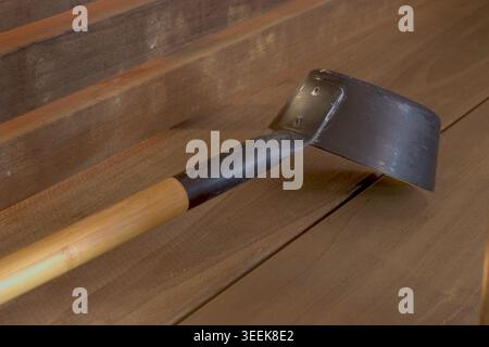Un moderno mestolo sauna in metallo nero con manico in legno appoggiato su una panca di legno scuro. L'immagine trasmette una cultura tradizionale della sauna finlandese. Foto Stock