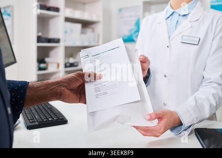 Primo piano del farmacista che consegna il pacchetto di ritiro della prescrizione a un uomo di mezza età al banco della farmacia, mostrando la dispensa di farmaci e il servizio ai pazienti per il marketing sanitario Foto Stock