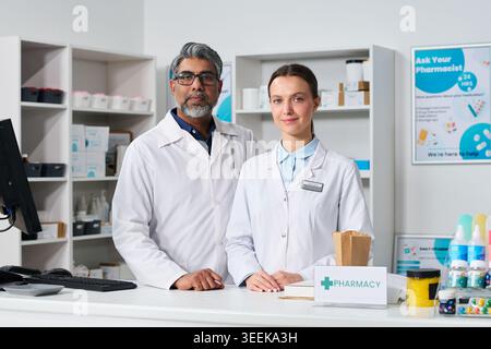 Ritratto dell'uomo indiano di mezza età e della giovane donna in piedi al banco della farmacia, al servizio dei clienti e che rappresenta il commercio al dettaglio e il supporto farmaceutico per il marketing della farmacia Foto Stock