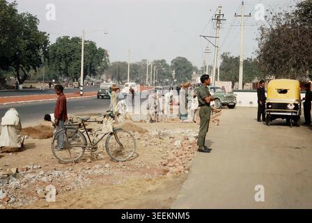 Un'istantanea a colori amatoriale di archivio dei primi anni '1970 che cattura un'intensa scena di strada a nuova Delhi, in India, con pedoni locali, una bicicletta parcheggiata, un ufficiale di polizia o un soldato che dirige il traffico e un risciò automatico sullo sfondo. Foto Stock