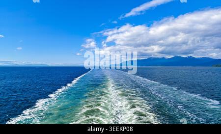 Alaska, Stati Uniti - 13 agosto 2024: Nave da crociera sveglia sul canale Lynn con vista sulle montagne lontane. Prelevato da una nave che viaggia sull'acqua vicino ad al Foto Stock