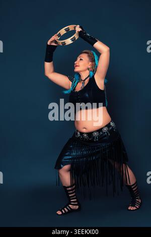 Donna allegra che si esibisce impegnandosi in danza percussiva, accompagnata da ritmici colpi di tamburello. Ballerina matura vestita di nero, manciata Foto Stock