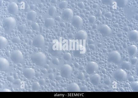 Sfondo astratto con numerose piccole e grandi perle d'acqua sparse su una superficie dai colori freddi Foto Stock