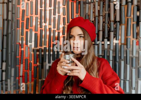 Donna berretto acqua elegante giovane donna in berretto rosso che tiene un bicchiere d'acqua in caffè con sfondo decorativo Foto Stock