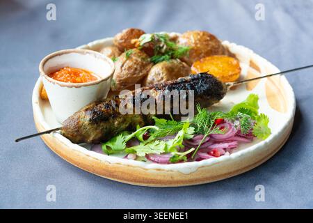 Piatto georgiano di lula kebab. Spiedino barbecue, piatto tradizionale barbecue con patate al forno e insalata. Souvlaki alla griglia, kebap di carne macinata, lula di montone su ta Foto Stock