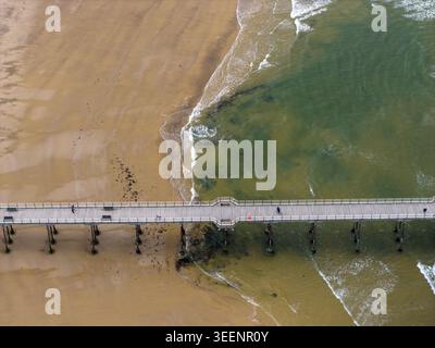 Vista aerea dall'alto verso il basso del molo di Saltburn accanto al litorale sabbioso e alle acque costiere poco profonde di Saltburn by the Sea nel North Yorkshire in Inghilterra durante lo stesso periodo Foto Stock