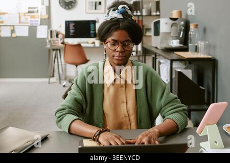 Donna adulta di colore che scrive alla scrivania nell'area di lavoro dell'ufficio domestico Foto Stock