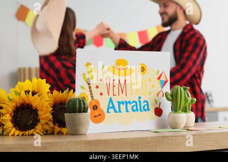 Biglietto d'auguri per la Festa Junina (Festival di giugno) e cactus in tavola contro coppia danzante in cucina, primo piano Foto Stock