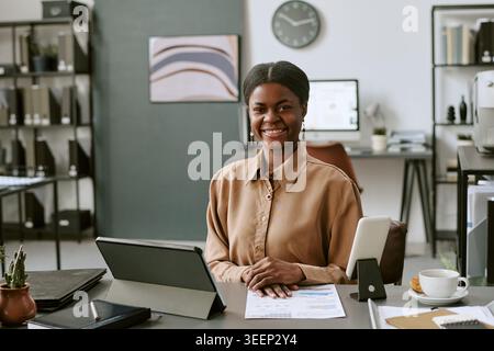 Ritratto di donna adulta nera seduta alla scrivania nell'ufficio moderno Foto Stock
