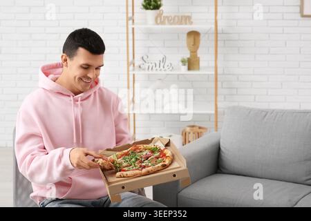 Giovane uomo che tiene in mano una scatola di cartone con gustosa pizza a casa Foto Stock