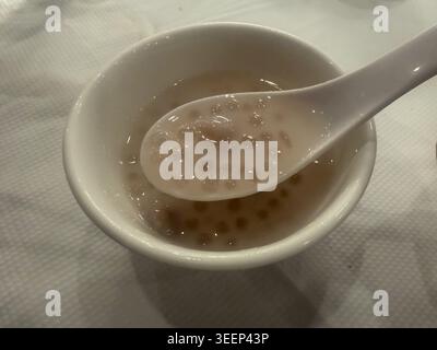 Cremosa zuppa di perle di tapioca servita in una ciotola bianca con cucchiaio di ceramica in un ristorante cinese. Foto Stock