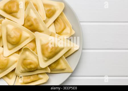 Ravioli triangolari freschi accatastati su un piatto in vista ravvicinata, evidenziando pasta setosa, consistenza fatta in casa e ripieno saporito. Ideale per ricette italiane Foto Stock