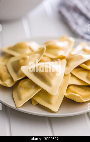 Ravioli triangolari freschi accatastati su un piatto in vista ravvicinata, evidenziando pasta setosa, consistenza fatta in casa e ripieno saporito. Ideale per ricette italiane Foto Stock