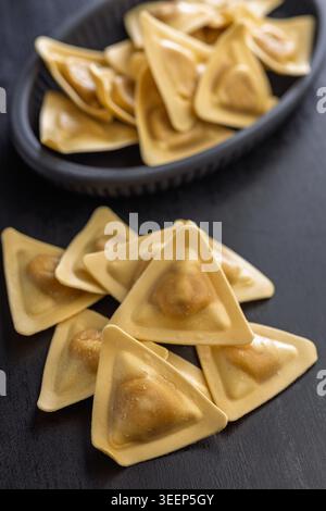 Primo piano di ravioli triangolari su una superficie di legno scuro, evidenziando la pasta ripiena cruda con impasto dorato. Ideale per la cucina italiana, ricetta visua Foto Stock